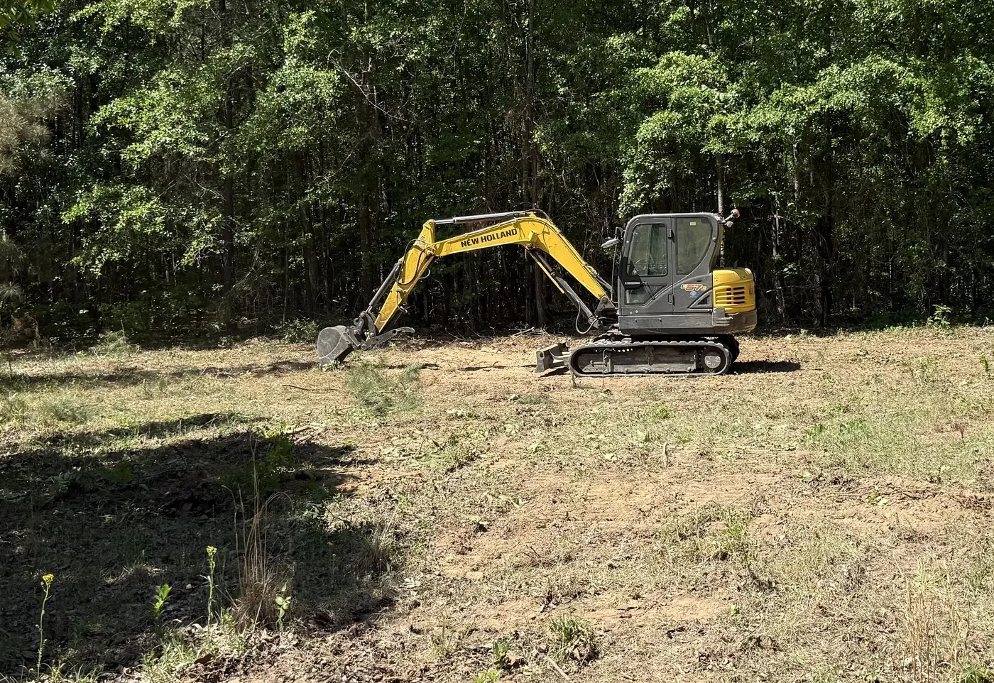 Mini excavator working at the tree line on a cleared lot