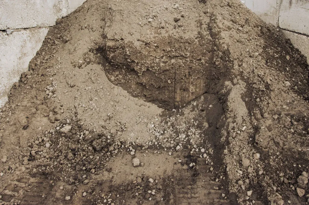 Close-up of a pile of fill dirt with small rocks mixed in, heaped against concrete block walls